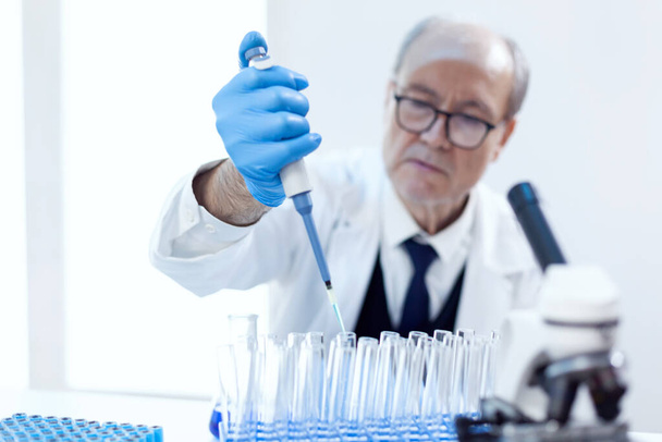 Φαρμακοποιός ρίχνει μπλε ουσία σε δοκιμαστικούς σωλήνες - Φωτογραφία, εικόνα