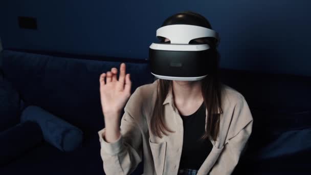  Young caucasian woman wearing VR helmet making hands gesture at home. Attractive woman enjoying virtual reality cyberspace. - Footage, Video