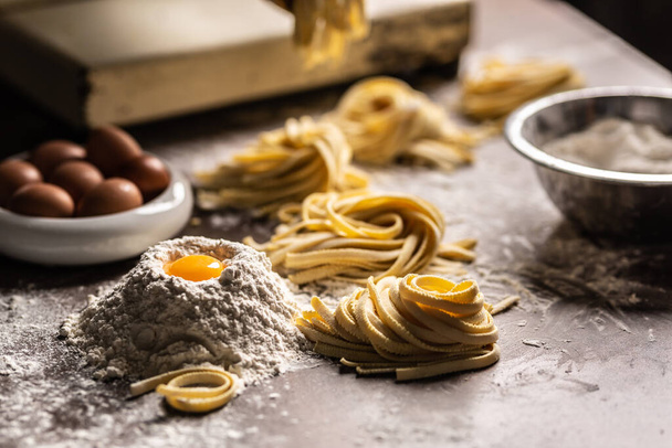 Nests of fresh fettuccine pasta with eggs, egg yolk, flour on a kitchen prep table. - 写真・画像