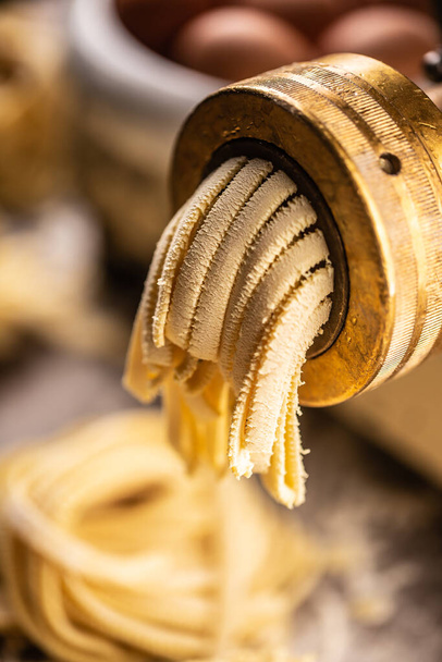 Detail of a pasta maker outlet with zigzagged edges fettuccine leaving it. - Valokuva, kuva