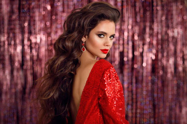 Beautiful brunette in red dress with Healthy wavy hair. Glamour Makeup. Fashion Beauty Girl Isolated on bright bokeh party Christmas Background.  - 写真・画像