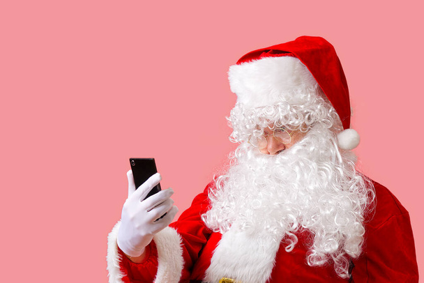 santa claus with mobile phone isolated on pink background - Photo, Image