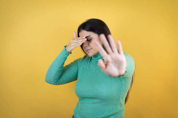 Young caucasian woman over isolated yellow background covering eyes with hands and doing stop gesture with sad and fear expression. Embarrassed and negative concept. - Zdjęcie, obraz