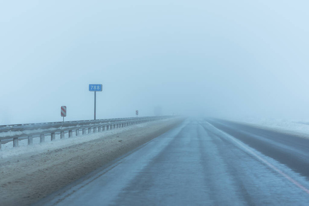 Lodowata droga z lodem i śnieżną mgłą. M4 autostrady don 788 km nieobrobione z lodu. Niebezpieczne i trudne warunki drogowe. Brudny śnieg na poboczu. Znaki drogowe wskazujące przebieg. Zimowe drogi w Rosji. - Zdjęcie, obraz