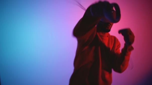 Młody człowiek z okularami VR na głowie walczący w wirtualnej rzeczywistości, robiący podbródek i wygrywający - Materiał filmowy, wideo