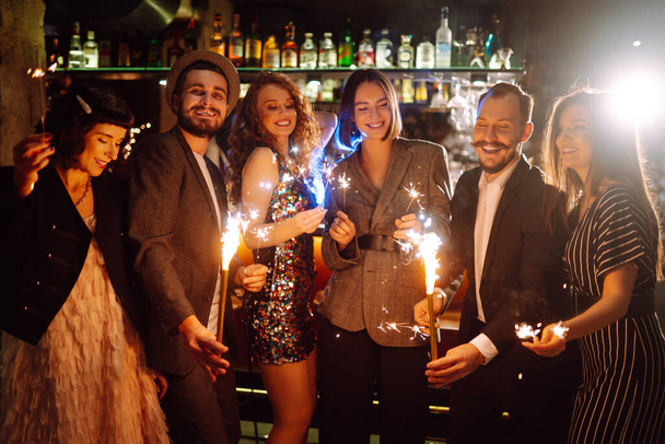 Friends celebrate Christmas or New Years party with sparklers and champagne. Group of happy people enjoying party with fireworks.Winter holiday, youth, lifestyle concept. - Photo, Image