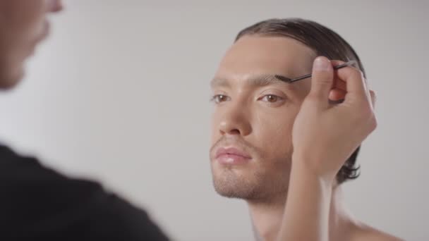 Lähikuva mies meikki taiteilija käyttäen spoolie harja ja kampaus kulmakarvat komea nuori mies - Materiaali, video