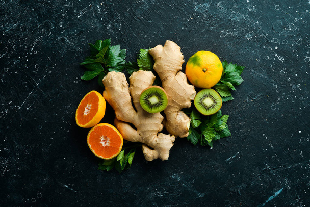 Vitamin C: Ginger, kiwi and tangerine on a black stone background. Top view. Rustic style. - Photo, image