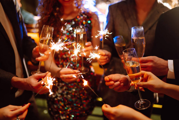 Glowing sparkles in hands. Group of happy people enjoying party with fireworks. Winter holiday, youth, lifestyle concept. - Foto, imagen