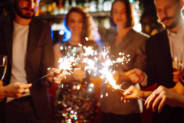 Glowing sparkles in hands. Group of happy people enjoying party with fireworks. Winter holiday, youth, lifestyle concept. - Photo, image
