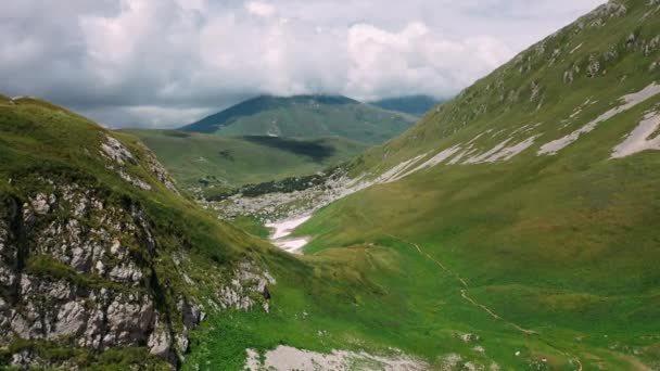Im Sommer fliegen wir über ein wunderschönes, mit Steinen und Schnee bedecktes Gebirgstal mit Gras unter herrlich schwebenden Wolken über dem kaukasischen Gebirge. Konzept von Ausflügen zu schönen Orten und Wanderungen - Filmmaterial, Video