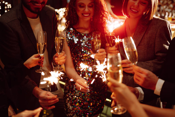 Glowing sparkles in hands. Group of happy people enjoying party with fireworks. Winter holiday, youth, lifestyle concept. - Photo, image