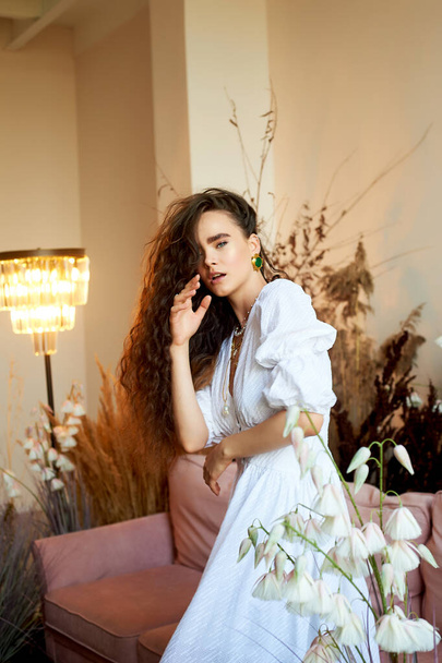 A beautiful girl with long curly hair in a white long dress, is moving dynamically. Photo studio with cereals. Fashion and beauty. - Foto, Imagem
