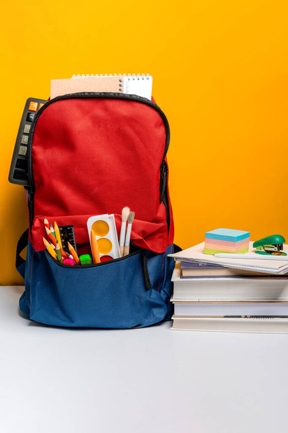 Schulrucksack mit verschiedenfarbigen Papeterie auf gelbem Hintergrund. Bannerdesign - Foto, Bild