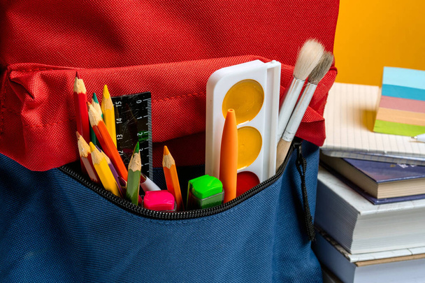 Plecak szkolny z różnym kolorowym papierem na żółtym tle. Projekt banera - Zdjęcie, obraz