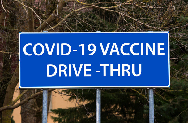  Covid-19 vakcína drive-thru koncept. Modrá značka ukazuje na cestu přes místo očkování. Manipulace s fotografií. - Fotografie, Obrázek