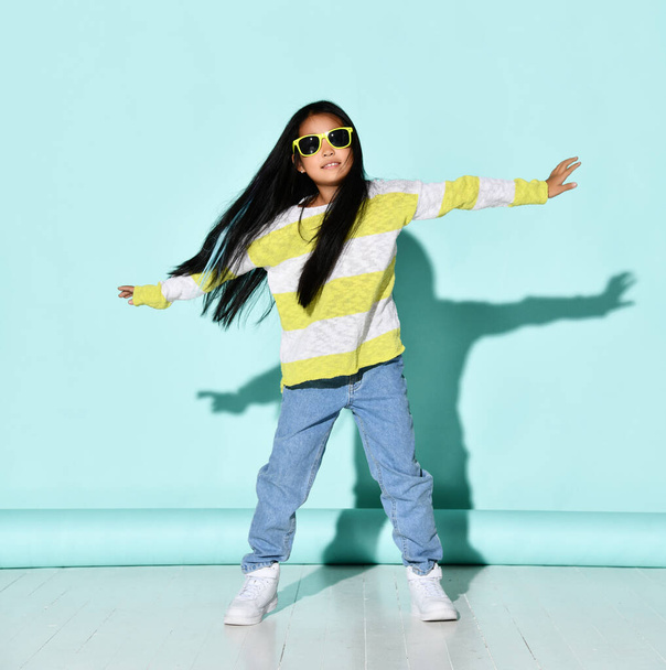 Portrait of a stylish bright Korean girl posing on a blue background with outstretched arms. - Foto, Imagen