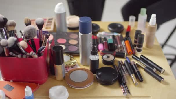 Korkea kulma laukaus tunnistamaton meikki taiteilija ottaa huulipunaa pöydästä täynnä kosmeettisia valmisteita ja työkaluja - Materiaali, video