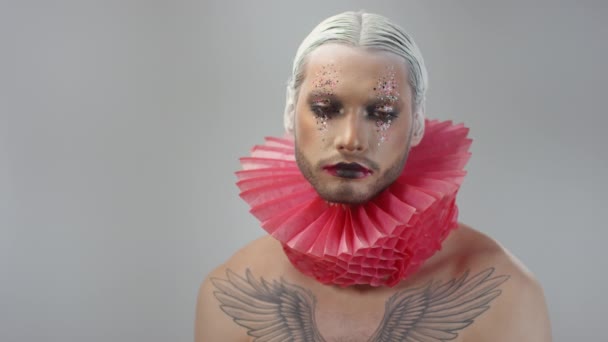 Portrait shot of handsome shirtless young man with full face of dramatic make-up, slicked back white hair and red ruff looking at camera - Footage, Video