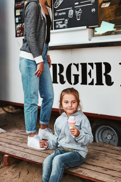 Little girl eating ice cream sitting on a step at front of food truck during family time on summer vacations - Photo, Image