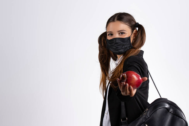 Tyttö koulupuvussa omena kädessään ja musta naamio. Koulutuksen ja terveydenhuollon käsite. Laadukas kuva - Valokuva, kuva