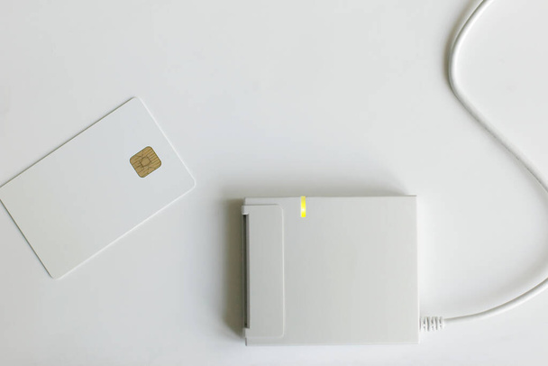 Um cartão de plástico branco e um leitor de dados pessoais. Roubo ou fuga de informações confidenciais. layout com espaço de cópia - Foto, Imagem