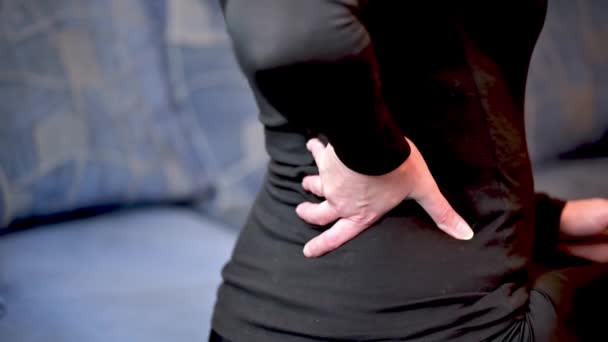 The woman rubs her back. A woman is sitting on the couch with back pain. - Footage, Video