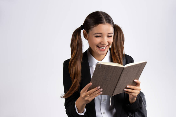 A cheerful schoolgirl reads a book and laughs. Interesting book, white background, blank space. High quality photo - Foto, imagen