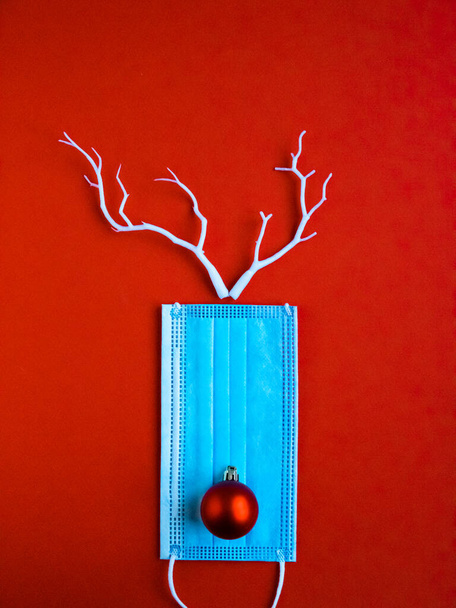 Festive christmas reindeer made from face mask and decorations. Christmas decoration of stars on red background with white blue masks for Covid and Coronavirus, Covid-19 concept - 写真・画像