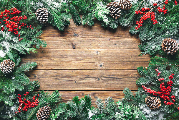 Christmas and New Year background with fir branches, holly and snowfall on wooden board - Fotografie, Obrázek