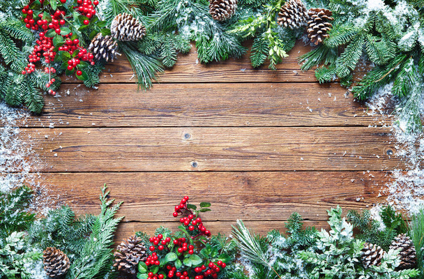 Christmas and New Year background with fir branches, holly and snowfall on wooden board - Fotografie, Obrázek