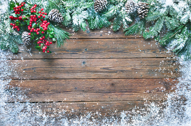 Christmas and New Year background with fir branches, holly and snowfall on wooden board - Photo, image
