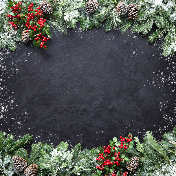 Christmas and New Year background with fir branches, holly and snowfall on dark stony board - 写真・画像