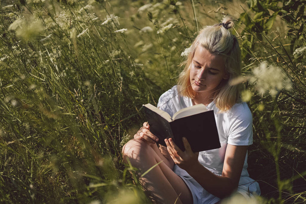 Tienermeisje die het boek in het veld leest. Het meisje dat op een gras zit en een boek leest..  - Foto, afbeelding