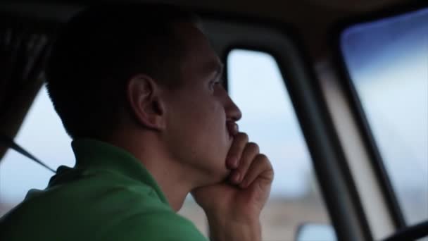 Egy fiatalember lehajtja a furgonját az országúton, és mereven bámul az útra, egyik kezén nyugvó fejjel. A kabinban. - Felvétel, videó