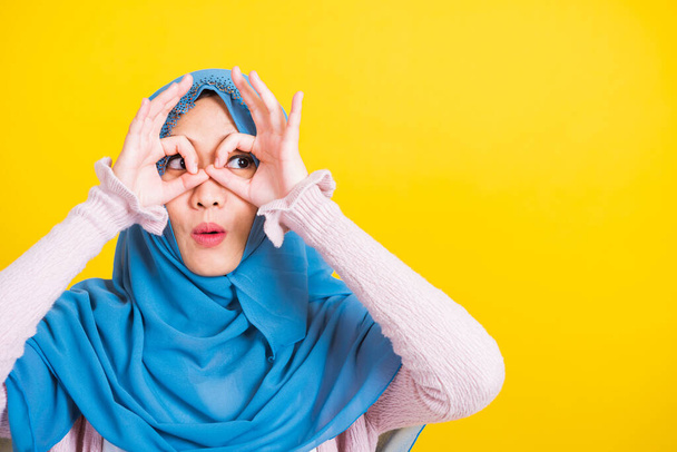 Asian Muslim Arab, Portrait of happy beautiful young woman Islam religious wear veil hijab funny smile she show gesture fingers in okay gesture symbol, OK sign over her eyes isolated yellow background - Фото, изображение