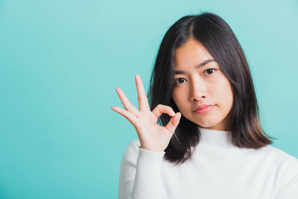 Young beautiful Asian woman smiling and showing hand the OK sign, Portrait female show finger okay gesture, studio shot isolated on a blue background - Foto, Imagen