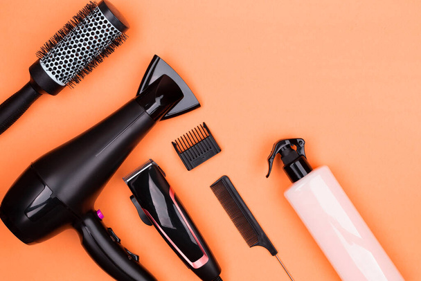 Hairdressing tools in black: hair dryer, combs, sprays, clipper on a orange background, place for text, flat lay. - Fotoğraf, Görsel