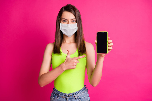 Photo of lady direct finger hold cell phone screen empty space wear white face mask isolated vibrant pink color background - Фото, зображення