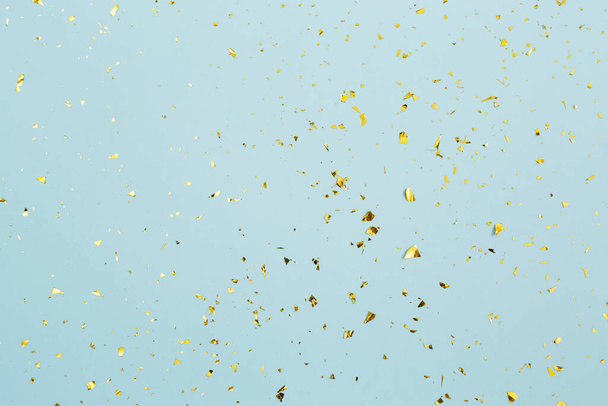 Golden confetti on light blue paper background. Festive holiday backdrop. Birthday congratulations Christmas New Year. Flat lay, top view, copy space. - Fotografie, Obrázek
