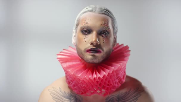 Portrait shot with moving light of shirtless young male model wearing theatrical make-up with glitter and red ruff around his neck posing for camera - Footage, Video