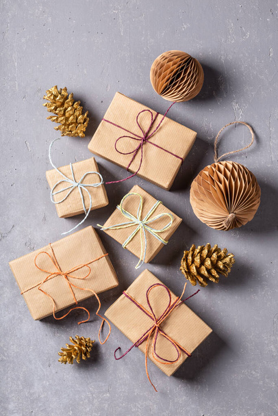 Kraft kağıdından hediyeler ve gri beton arka planda çevre dostu dekorasyonlarla yapılmış şenlikli bir Noel kompozisyonu. Noel israfı. - Fotoğraf, Görsel