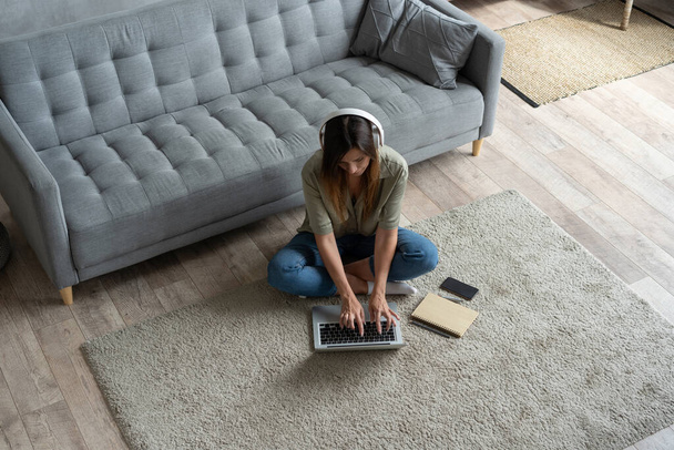 Просто вдохновил. Уверенная молодая красивая улыбающаяся женщина, работающая на ноутбуке, сидя дома на полу. - Фото, изображение