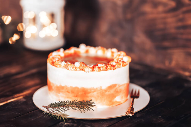 Cake on a white plate with a fork. Sweets for any holiday. On a wooden background with garlands and a lantern. - Foto, immagini