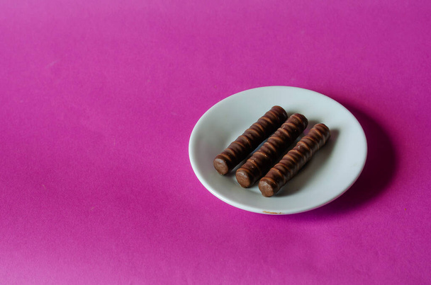 Three chocolates in white saucer on pink background. Sweet treats and candy wrapper on colored surface. Confectionery - Foto, afbeelding
