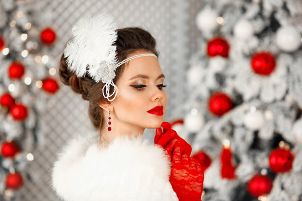 Retro woman portrait in fur coat. Elegant brunette woman with feather in wedding hairstyle, beauty makeup and ruby jewelry set wears posing over Christmas tree background - Photo, image