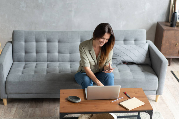 Woman using laptop and mobile phone on sofa. - Foto, Bild