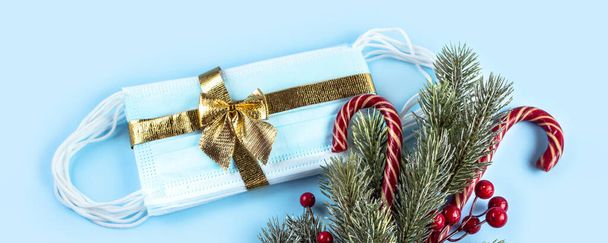 Medizinische Schutzmasken mit goldenem Band auf blauem Hintergrund mit Tannenzweig und Weihnachtsschmuck. Ein Geschenk zu Weihnachten und Neujahr 2021. Coronavirus-Pandemiekonzept. Banner. - Foto, Bild