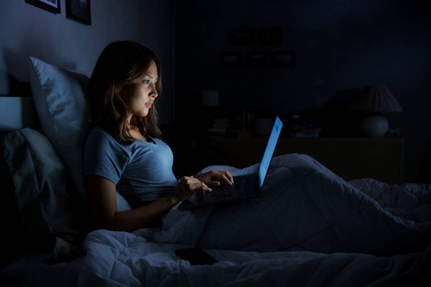 Young woman using a laptop in her bed at night - Fotografie, Obrázek