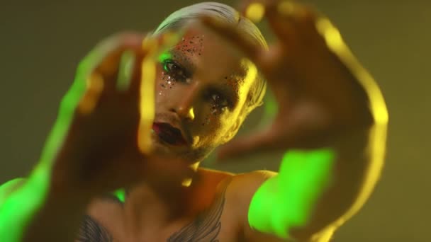 Portrait of shirtless young man with bold make-up with glitter and white hair posing for camera - Footage, Video